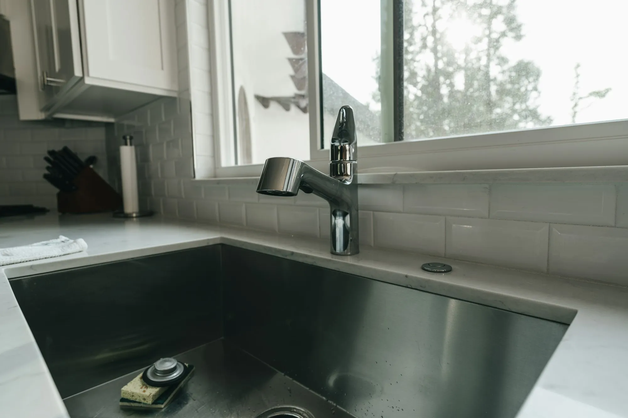 Local Water Experts Who Test First and Sell Second Kitchen faucet over a stainless sink beside a sunny window